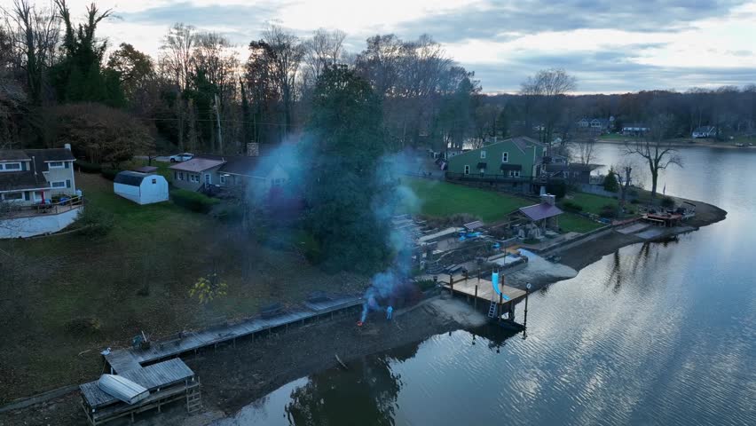 Aerial view of an American lakeside residential community in late autumn, with houses, docks, calm water and light smoke rising near shoreline under cloudy evening sky usa. Top view.