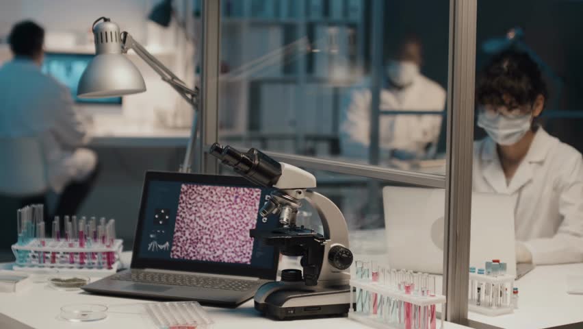 A fast-paced timelapse showing a modern clinician’s workspace with a laptop, microscope, and test tubes, capturing the dynamic rhythm of a busy medical lab.