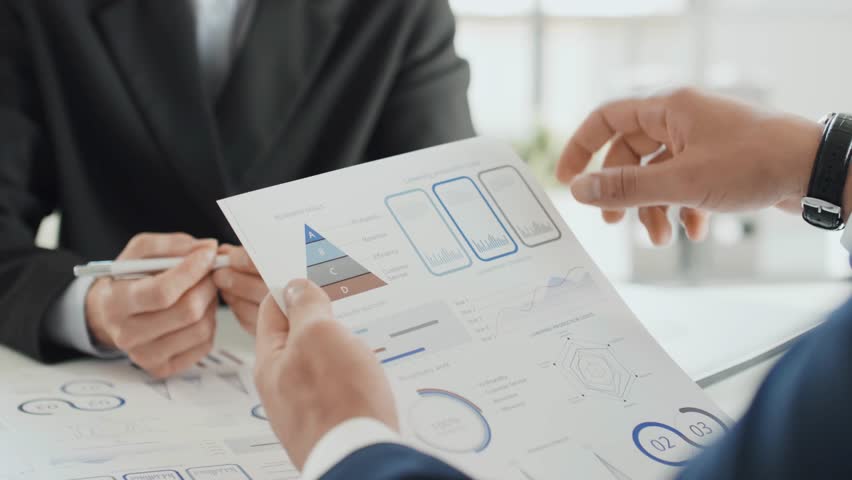 Over-shoulder cropped slow-motion shot of two unrecognizable business partners discussing a project. Professional teamwork, corporate collaboration, and office discussion captured in detail.