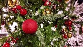 Single matte red bauble on green Christmas pine tree, showing fine details of needles, shiny gold baubles, red berries and hints of white snow-like flocking in the background bokeh, slow motion pan - Powered by Shutterstock - Get 15% off with code: PIKWIZARD15