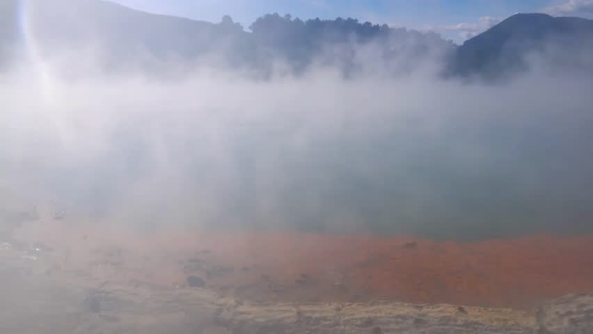 Steam rises from the Champagne Pool hot spring with vibrant blue water and orpiment deposits, showcasing a striking geothermal landscape in nature.