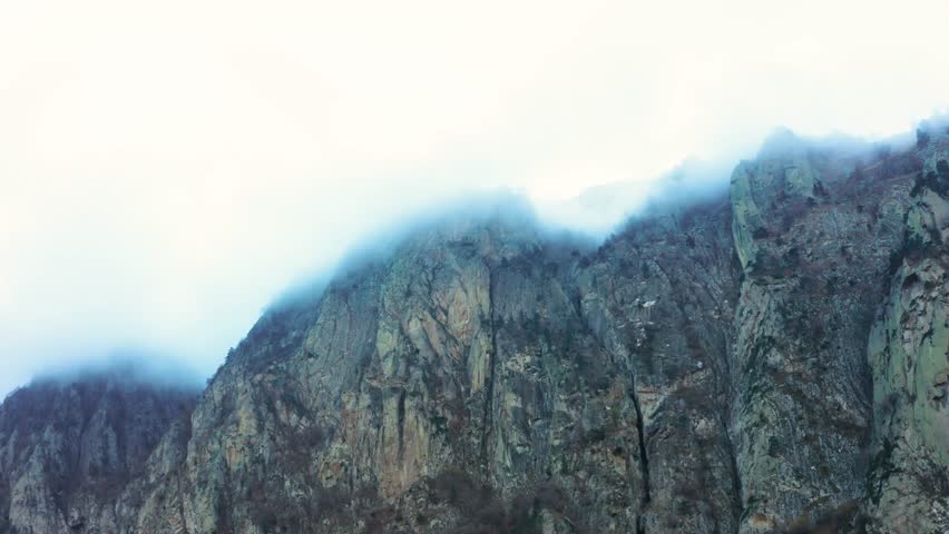 A view of the rugged, rocky peaks of the North Caucasus mountains partially shrouded in mist and clouds. The dramatic landscape showcases the raw beauty and majestic scale of the Russian countryside,