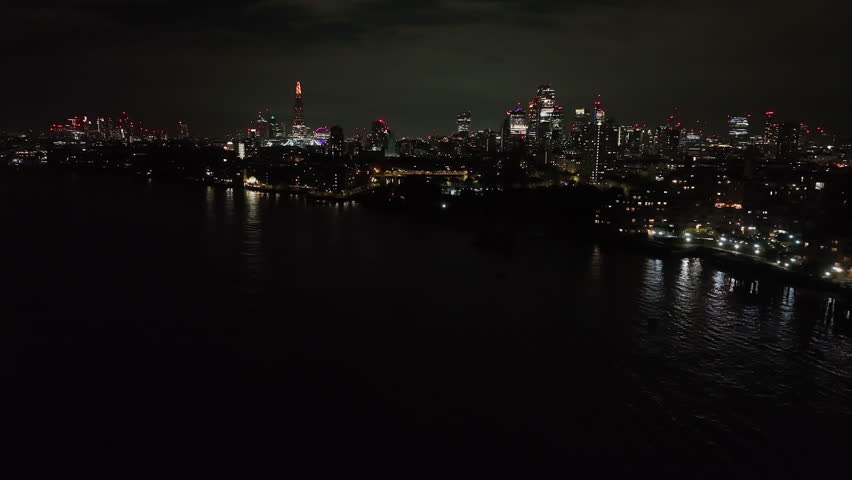 Aerial view rising over Thames river, toward the skyline of London, night in UK