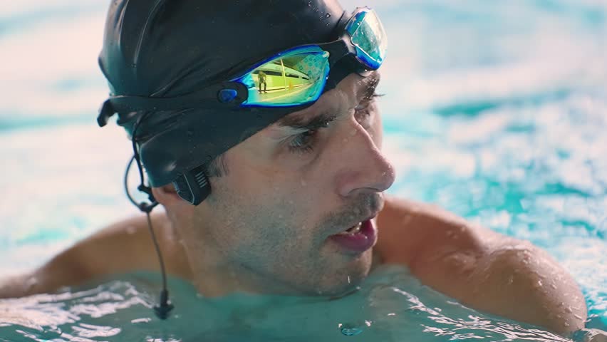 A focused swimmer pauses to catch his breath in the pool, showcasing determination and concentration as he prepares for the next lap in a competitive swimming environment.