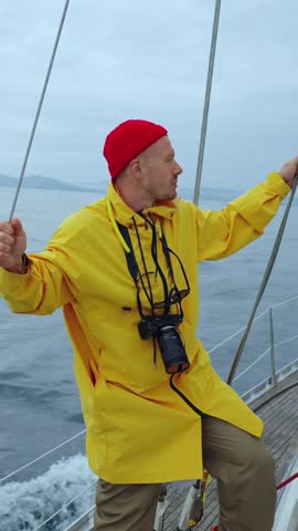 A Focused Sailor in a Bright Yellow Raincoat Capturing Moments on the Deck Amidst Serene Waters Under a Cloudy Sky