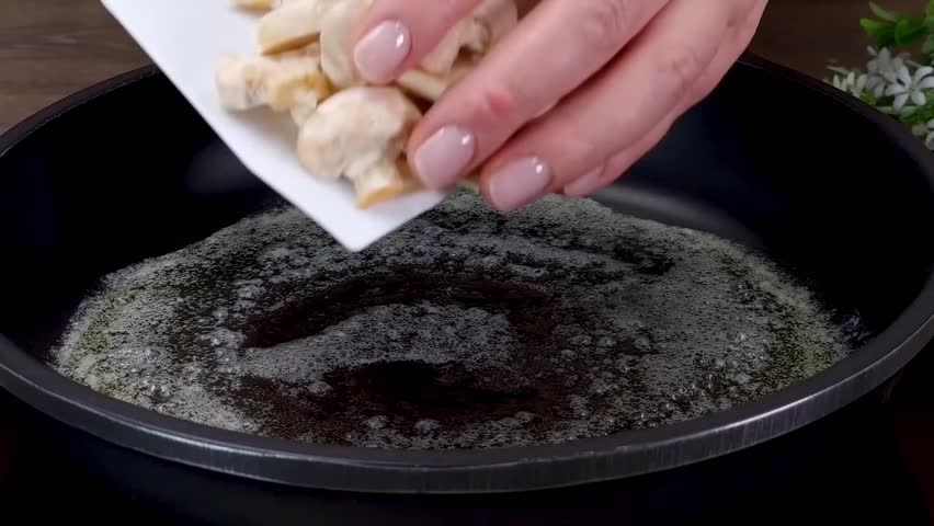 Sauteing sliced white button mushrooms in melted butter on a frying pan during food preparation
