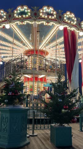 Bright spinning Christmas carousel illuminated with numerous colorful festive lights at night. Magical holiday atmosphere, glowing decorations, cheerful winter fair mood captured in motion