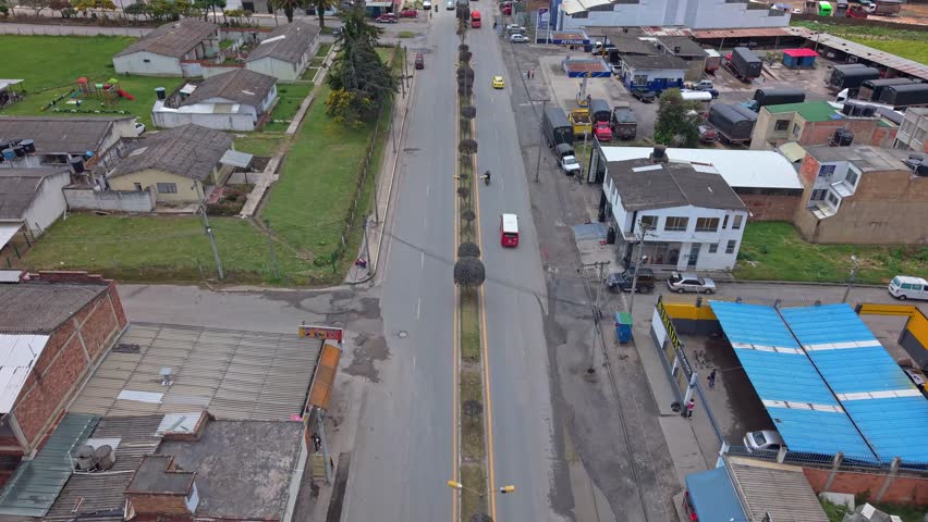 Static aerial view of a main road in Chiquinquirá, Colombia, showing cars moving along the central avenue and surrounding residential and commercial buildings.