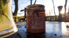 Close up shot of a rustic jar labelled Frosted Pumpkin Pie resting on a reflective wooden table outdoors with sunlight and trees in the background - Powered by Shutterstock - Get 15% off with code: PIKWIZARD15