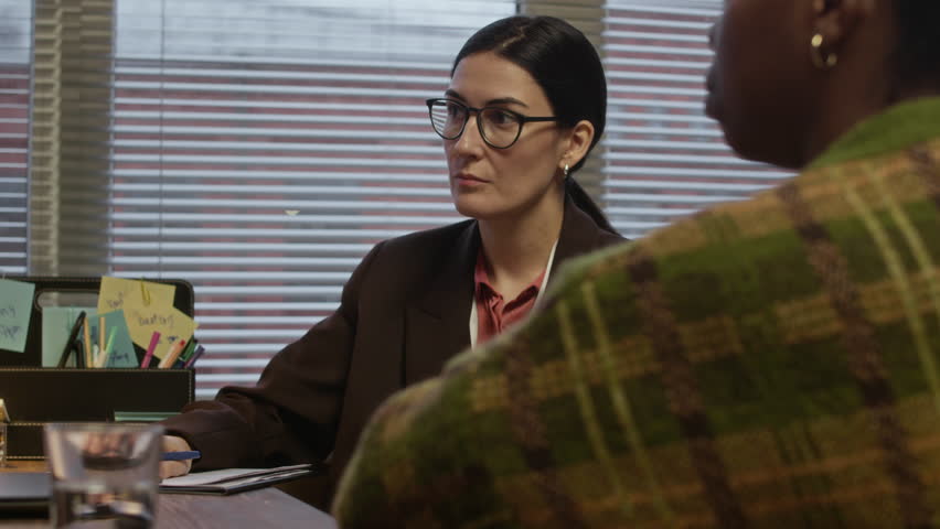 Medium shot of female Caucasian counselor taking notes while having appointment with black woman in office