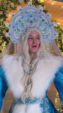 Vertical video of Snow Maiden, against the backdrop of a decorated winter house, claps her hands and smiles in a traditional costume.