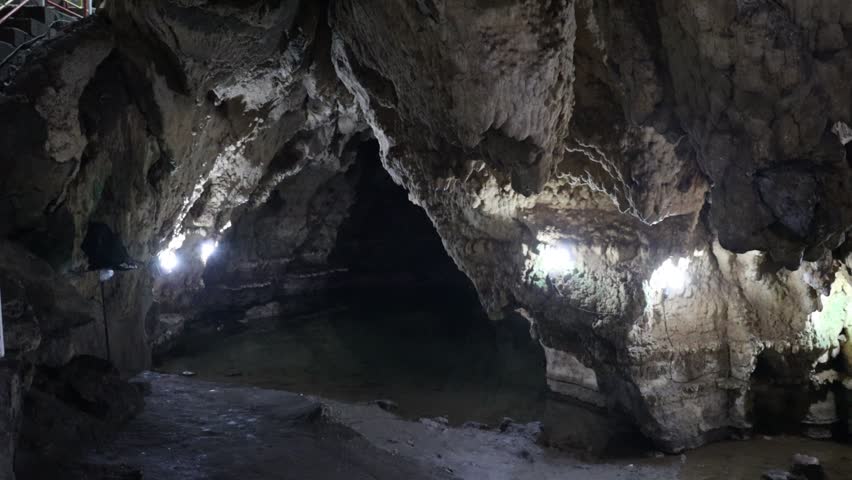 "Moving view inside a dim natural cave with rocky walls, textured surfaces, and soft ambient reflections, forming a quiet underground scene suitable for commercial nature footage."