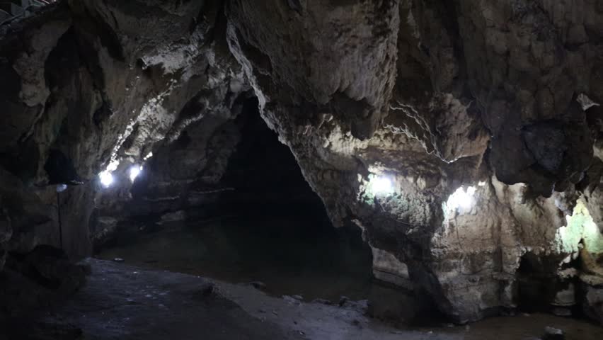 "Moving view inside a dim natural cave with rocky walls, textured surfaces, and soft ambient reflections, forming a quiet underground scene suitable for commercial nature footage."