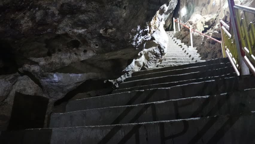 "Moving view inside a dim natural cave with rocky walls, textured surfaces, and soft ambient reflections, forming a quiet underground scene suitable for commercial nature footage."