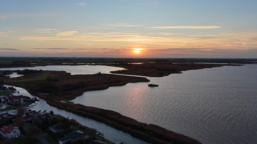 Soft sunrise over Dutch wetlands with winding water channels, calm reflective lakes, golden sky tones and wide flat landscape. Peaceful early-morning atmosphere in Europe. Drone ascend wide shot.
