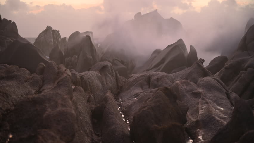 Dramatic Twilight View of Granite Rocks in Sardinia as Powerful Storm Waves Crash and Create Misty Sea Spray Along the Rugged Coastline