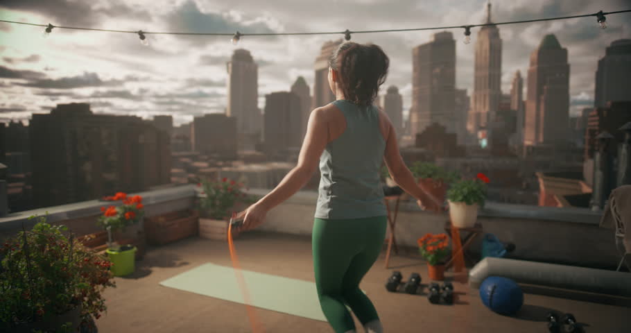Young Woman Practices Jump Rope Exercise on Rooftop Workout Space, Using Gear for Sport, Daily Fitness, Heart Health, and Calm, Mindful Movement with City in Background