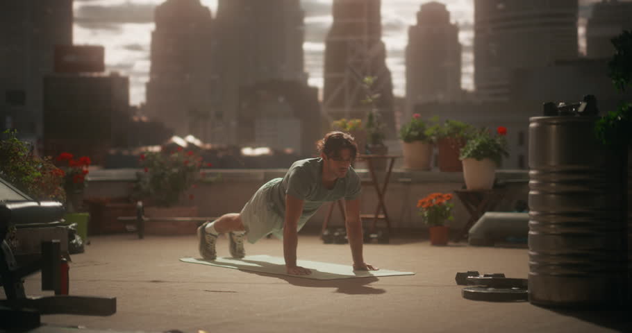 Man Holds a Steady Plank and Lowers Into Slow, Pushups on a Rooftop Mat, Using Bodyweight Strength Training to Build Chest, Arm, Core Power During an Intense Solo Outdoor Workout Session.