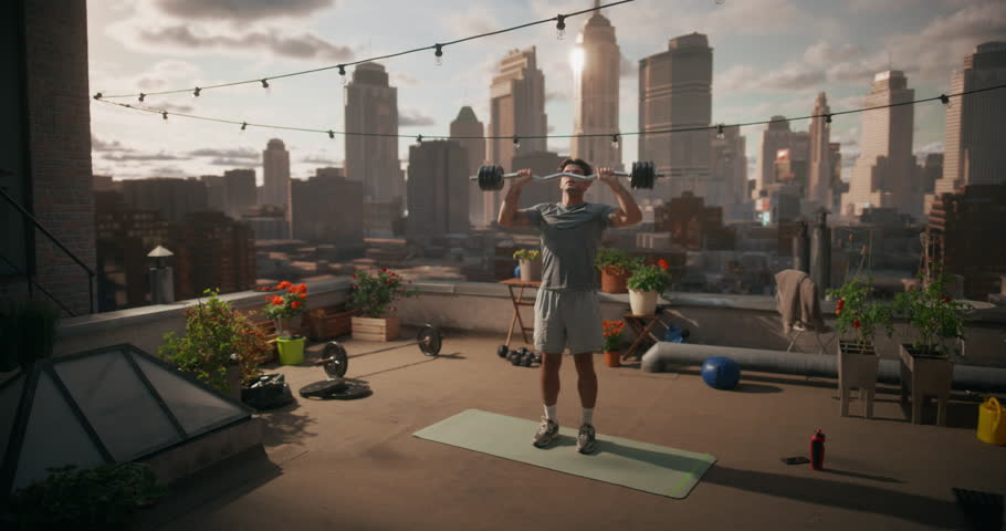 Young Man Stands on a Rooftop Doing Standing Ez Bar Shoulder Presses, Lifting the Weight Overhead for Strength Training, Upper Body Fitness, Health Care Exercise with City View