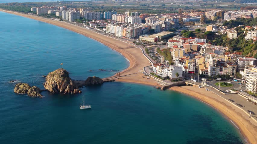 Magnificent aerial view showing the coastal town of blanes with its famous sa palomera rock, separating the bay from the long sandy beach, a popular summer destination in costa brava, spain