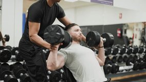 Dedicated personal trainer coaching and spotting a male athlete performing an intense incline dumbbell press for chest and shoulder development - Powered by Shutterstock - Get 15% off with code: PIKWIZARD15
