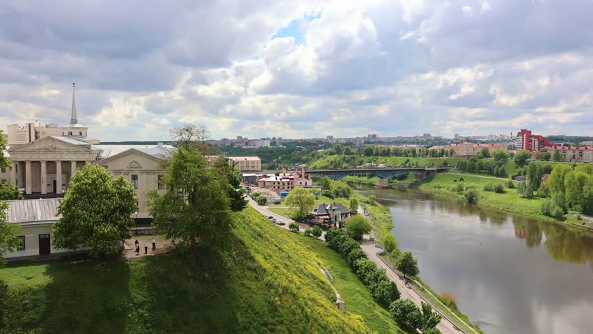 Panoramic view of Grodno city with river, green slopes and historic buildings under cloudy sky, taken handheld. High quality 4k footage