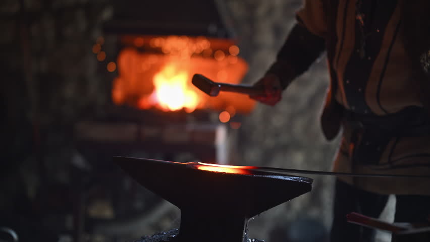 A Viking blacksmith with a white beard and braided hair works intently at a forge, hammering glowing metal on an anvil, with flames flickering in the background of a stone workshop cinematic slow