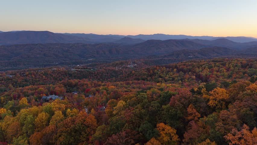 Aerial panoramic movement of autumn forest in fall with distant mountains during sunset glow in the USA.