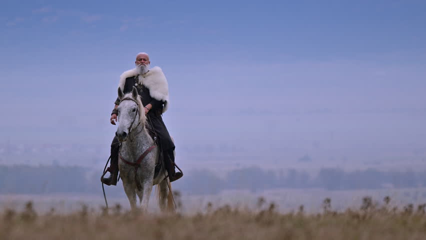 Elderly Viking warrior in fur cloak riding gray horse across open field at sunrise, mountains and distant cross behind him, moody cinematic Norse atmosphere cinematic slow motion 