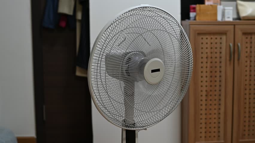 Electric standing fan oscillating, creating a rhythmic motor humming, mechanical clicking, and light air whistling sound.