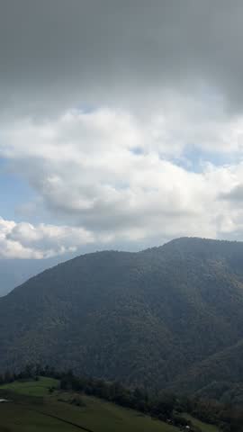 Man standing on a mountain viewpoint, looking out over a vast landscape covered in green hills and distant ridges.