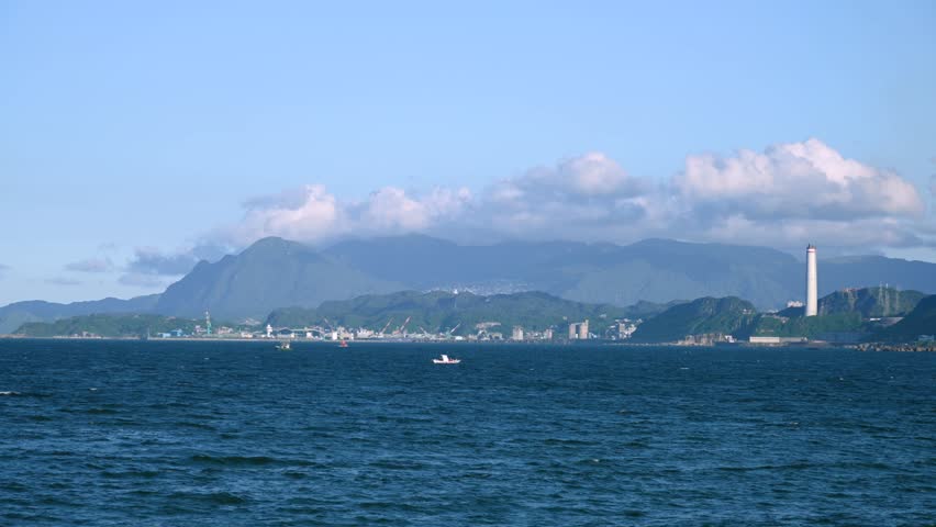 Winter afternoon serene sea view from Guihou Fishing Harbor in Wanli New Taipei Taiwan with boat to distant Keelung city tall power plant chimney port and green mountains under clouds.