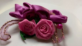 Rotating footage of a handmade satin floral accessory in pink and purple, showcasing detailed ribbon petals, beads, and elegant craftsmanship. Perfect for craft, fashion, and decorative themes - Powered by Shutterstock - Get 15% off with code: PIKWIZARD15