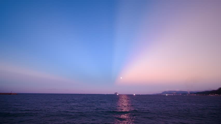 Winter dusk moon rising with pink purple sky reflection on calm sea Keelung Islet silhouette from Guihou Fishing Harbor Wanli New Taipei Taiwan.