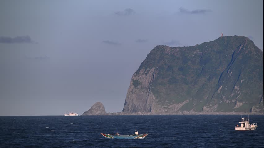 Scenic twilight view of Keelung Islet near Guihou Fishing Harbor Wanli New Taipei City Taiwan. Beautiful sunset sky colors. Fishing boat and large cargo ship sailing on the sea.