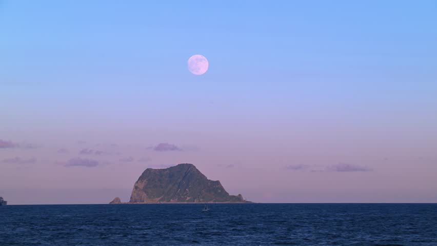 A beautiful moon rise over Keelung Islet near Guihou Fishing Harbor Wanli New Taipei City Taiwan at sunset. Ships and fishing boat on the calm ocean.