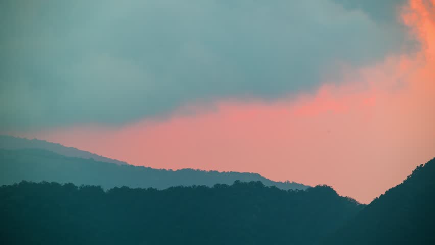 Close up of a giant orange sun setting over the dark mountain range silhouette on a winter afternoon in Ruifang, New Taipei City, Taiwan. Dramatic nature background.