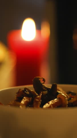 A hand skillfully uses chopsticks to lift food from a white bowl. Soft candlelight creates a cozy atmosphere, enhancing the intimate dinner experience at home