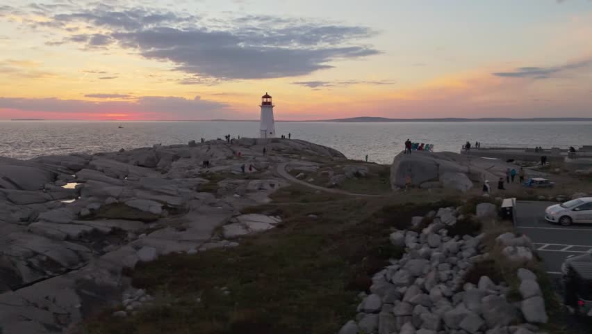 Cinematic Aerial View Of The Historic Peggys Cove Lighthouse Near Halifax, Nova Scotia, Standing On Rugged Granite Rocks At Sunset, With Warm Light Reflecting On The Wet Stone Surface And The Atlantic