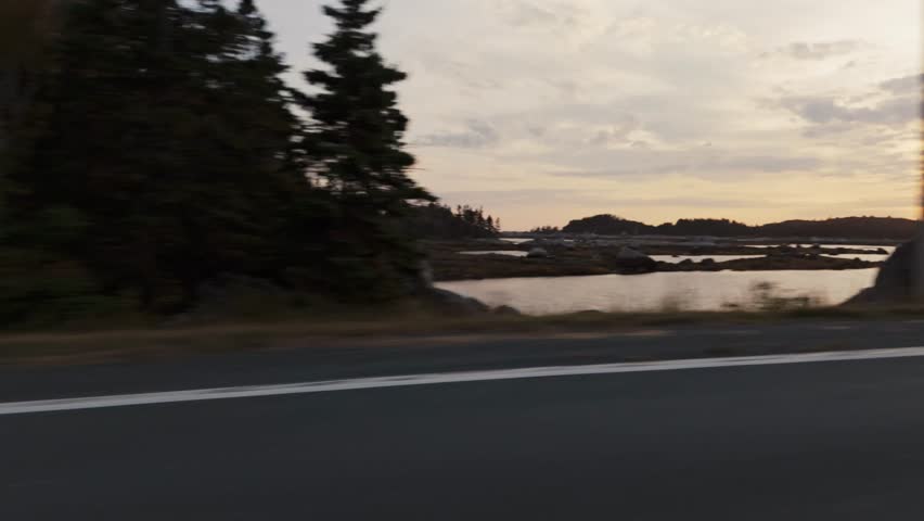 POV View From Inside A Moving Car Along A Highway Near Peggys Cove In Halifax, Nova Scotia, Capturing The Rocky Atlantic Ocean Shoreline At Dusk, With Soft Sunset Colors Reflecting Over The Coastal 