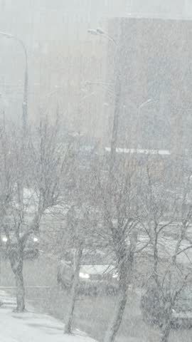 Heavy snowfall in city street with cars and trees