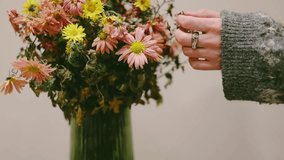 A woman's hand with a massive silver ring on a finger in a grey knitted sweater, holding a lush autumn bouquet of chrysanthemums in warm tones. The orange, yellow flowers create a cozy, autumnal scene - Powered by Shutterstock - Get 15% off with code: PIKWIZARD15