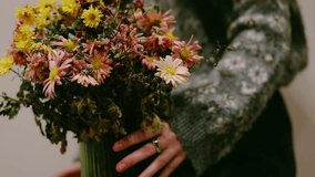 A woman's hand with a massive silver ring on a finger in a grey knitted sweater, holding a lush autumn bouquet of chrysanthemums in warm tones. The orange, yellow flowers create a cozy, autumnal scene - Powered by Shutterstock - Get 15% off with code: PIKWIZARD15