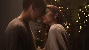 Romantic evening moment as a couple leans in for a tender near-kiss and then kisses, surrounded by cinematic warm Christmas lights and a decorated tree creating a cozy festive atmosphere. - Powered by Shutterstock - Get 15% off with code: PIKWIZARD15