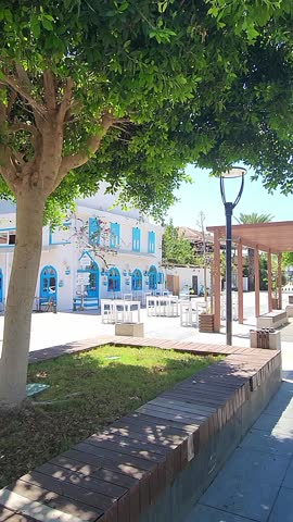 Bright outdoor patio with white building and blue window frames surrounded by greenery, Demre, Turkey, taken handheld, vertical video. High quality FullHD footage