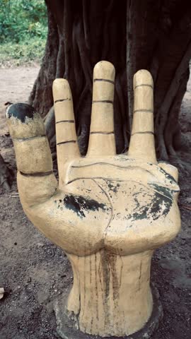 A carved wooden hand sculpture beside a tree trunk, showing rugged texture and craftsmanship in an outdoor setting.