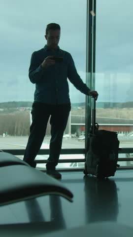 man gazes outside through terminal glass, individual waits calmly with scenic runway view behind him