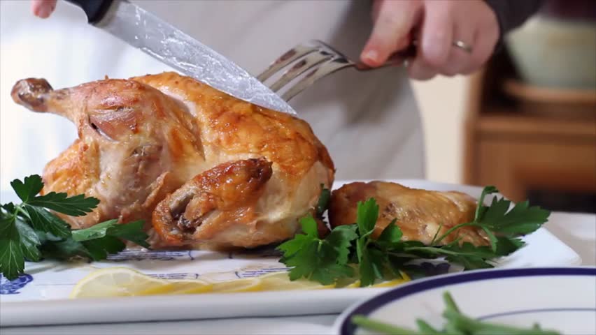 Closeup of hands carving a roasted chicken on a plate, highlighting food preparation, cooking, and delicious meal presentation.