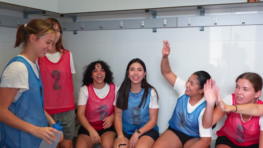 Cheerful female football players celebrating victory and high fiving each other in the locker room. Team bonding after a successful match