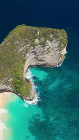 Trendy aerial drone shot of iconic Kelingking Beach cliffs on Nusa Penida, Bali, showing emerald sea, white sand and rugged rock. Perfect for travel promos, destination ads, vlogs, social media.
